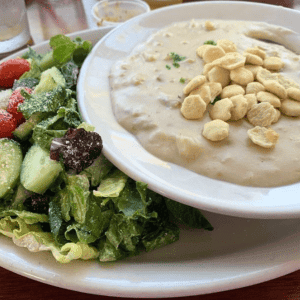 A bowl of Brophy Bros clam chowder with oyster crackers sits next to a mixed green salad garnished with fresh tomatoes and cucumbers.