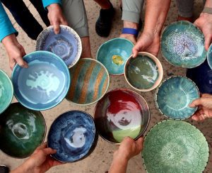 A group of hands holding various colorful, handcrafted ceramic bowls in a circle.