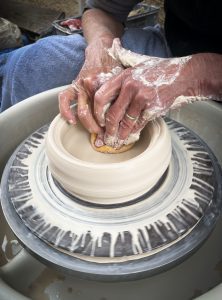 Person shaping clay on a pottery wheel, focusing intently on forming the vase. Hands covered in white clay.