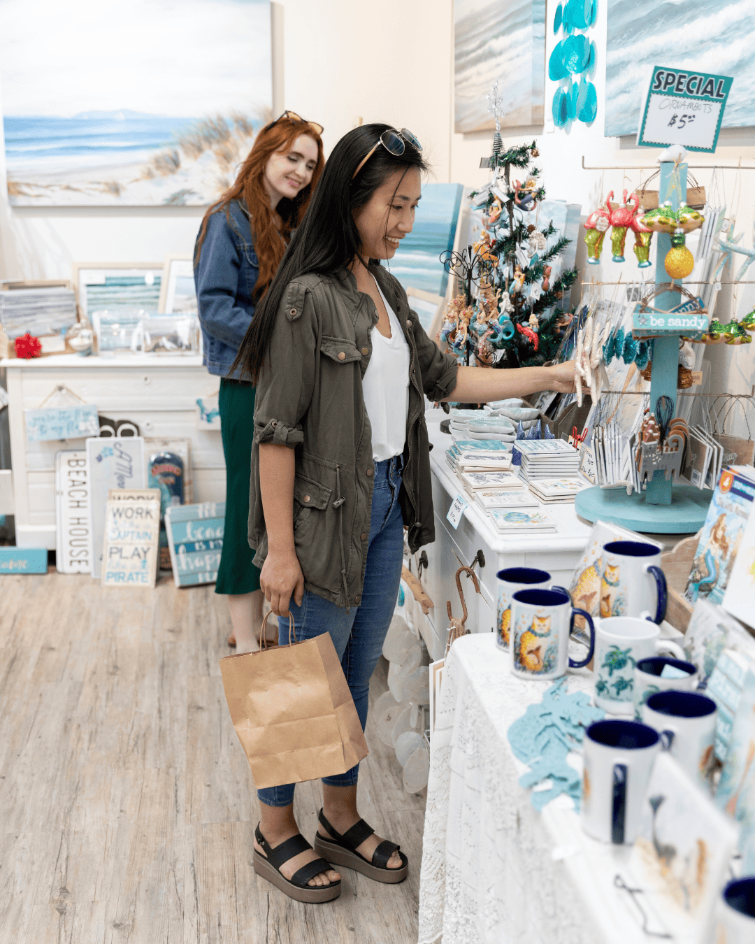 Two women shopping at Ventura Harbor Village holiday store with beach-themed decor.