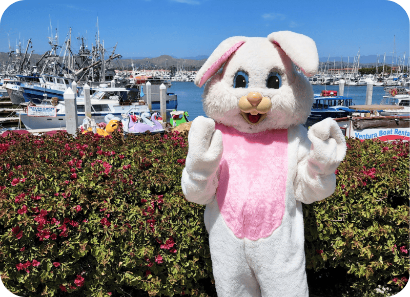 Easter bunny mascot at Ventura Harbor Village during spring celebration with boats in background.