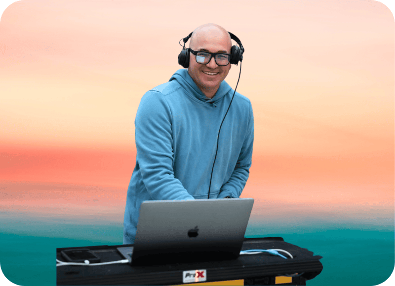 DJ performing outdoors at sunset with laptop and headphones in Ventura Harbor.