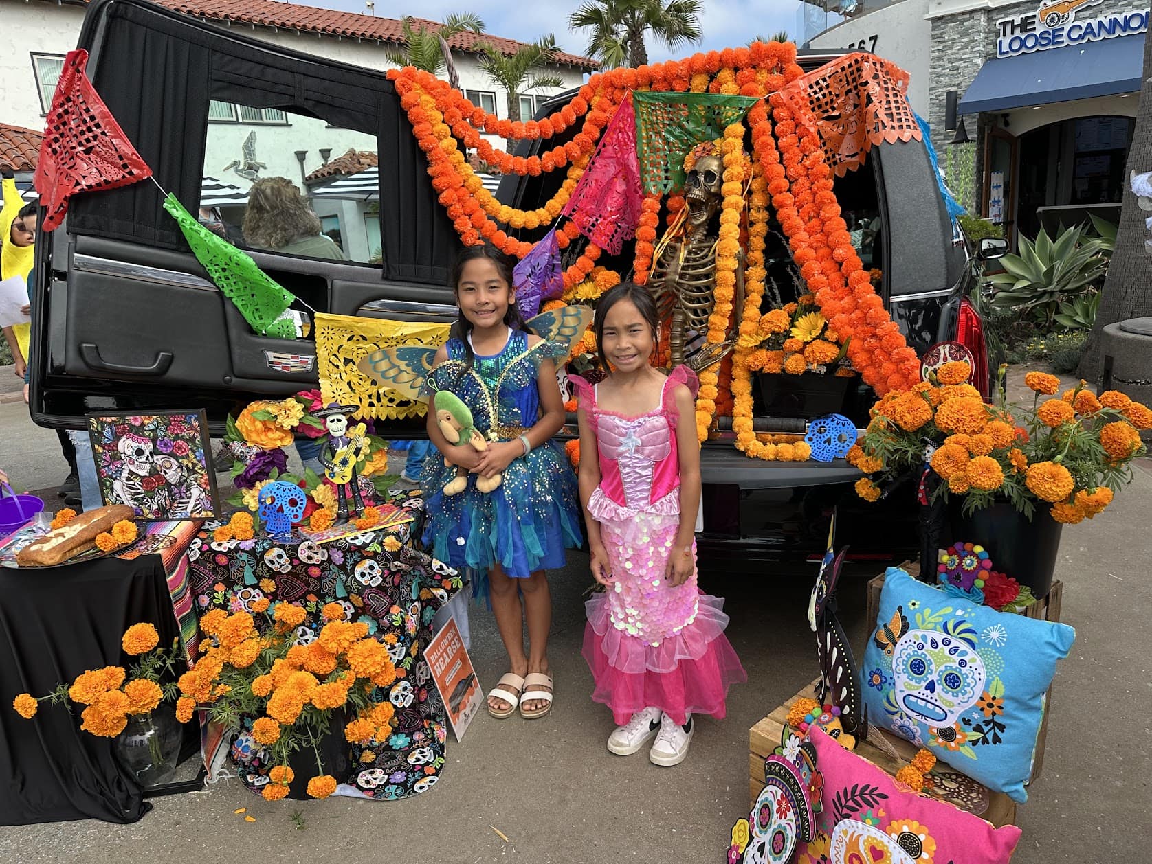 Two girls in colorful costumes stand near a decorated float at Ventura Harbor Village during Seaside.