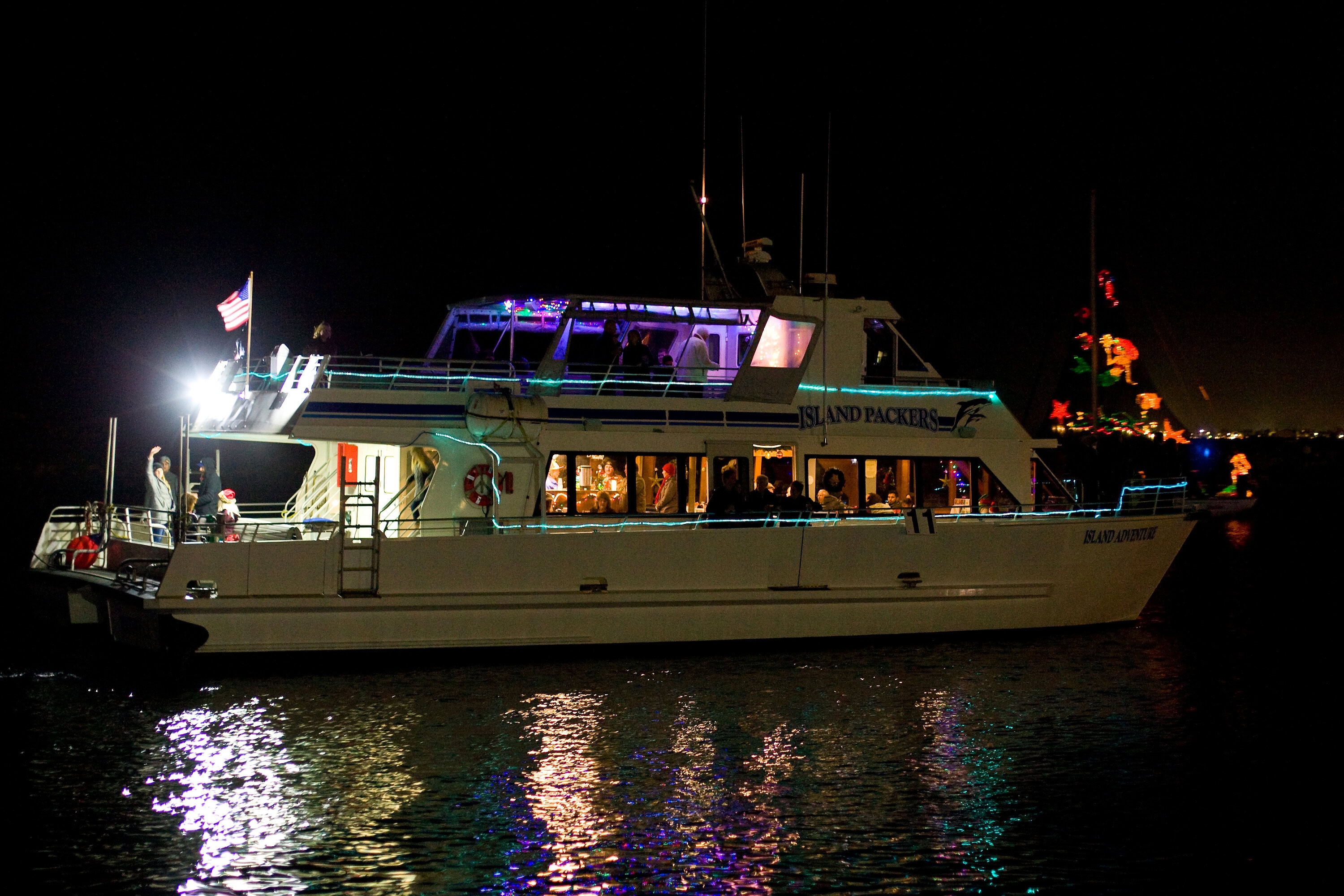 Nighttime boat cruise at Ventura Harbor Village with festive lights and reflections.