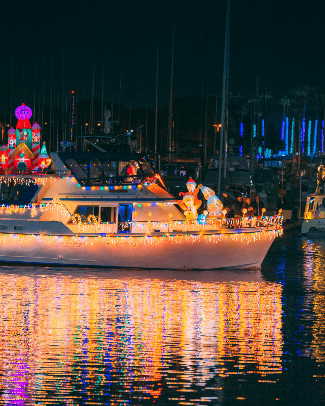 Festively decorated boat with Christmas figures and lights at Ventura Harbor at night.